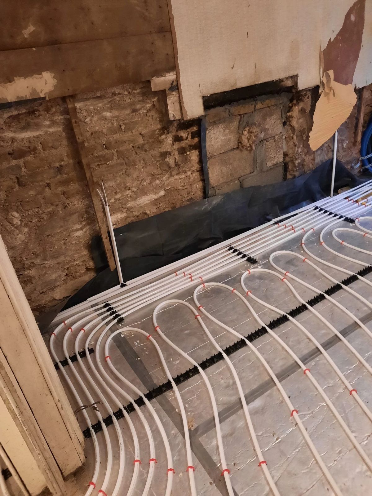 Underfloor heating pipes laid beside an old stone wall
